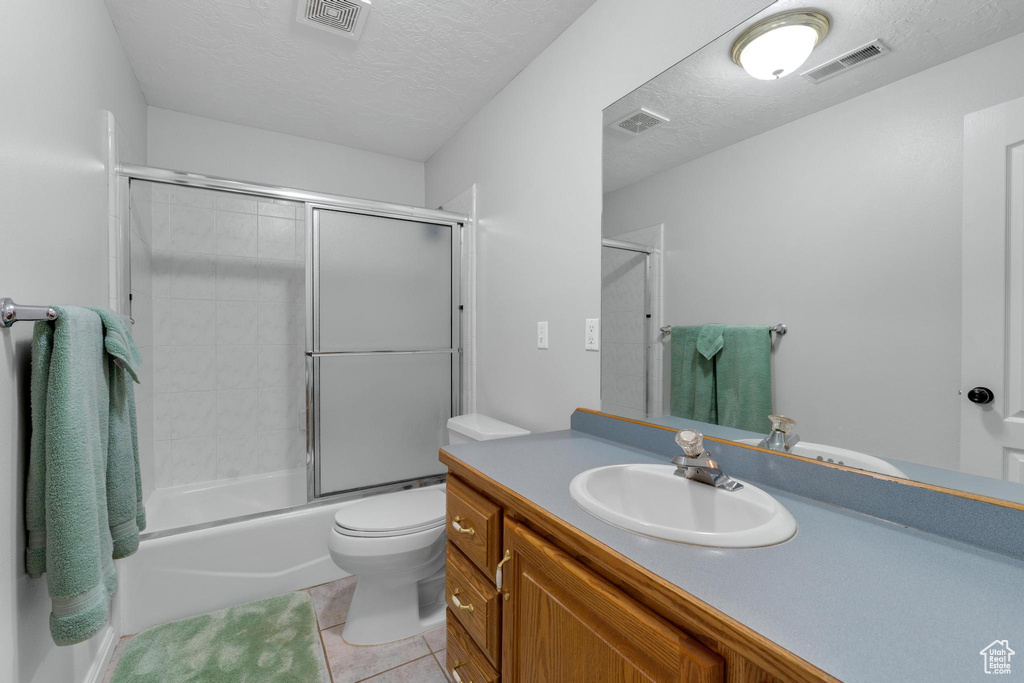 Full bathroom with vanity, a textured ceiling, tile flooring, toilet, and enclosed tub / shower combo