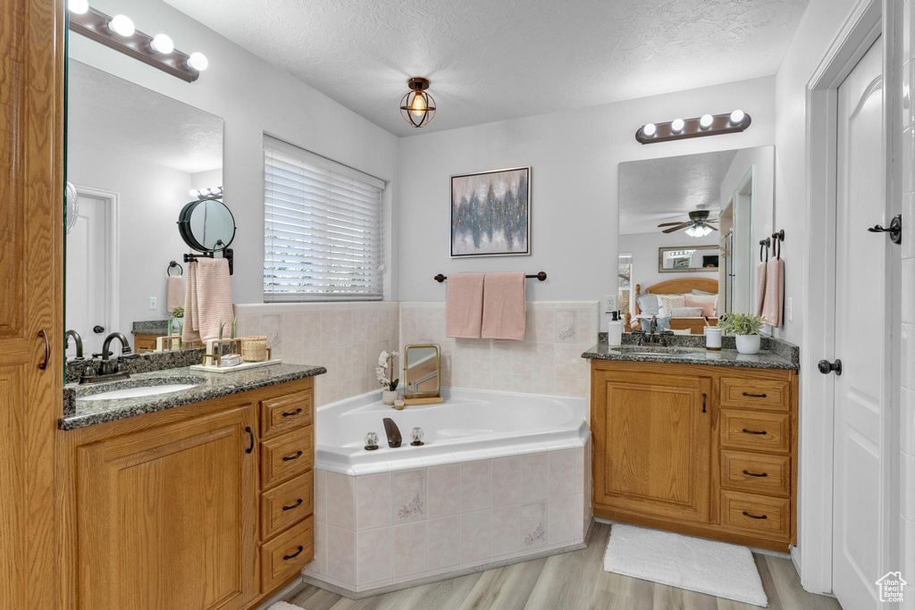Bathroom with hardwood / wood-style flooring, ceiling fan, a textured ceiling, dual bowl vanity, and a relaxing tiled bath