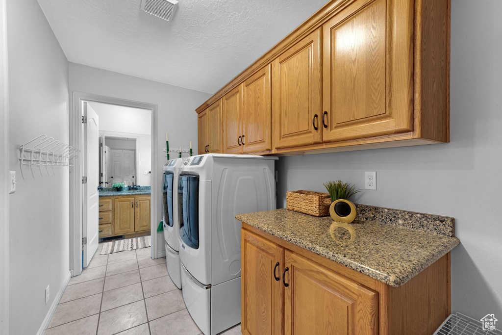 Laundry room featuring light tile floors, cabinets, and separate washer and dryer