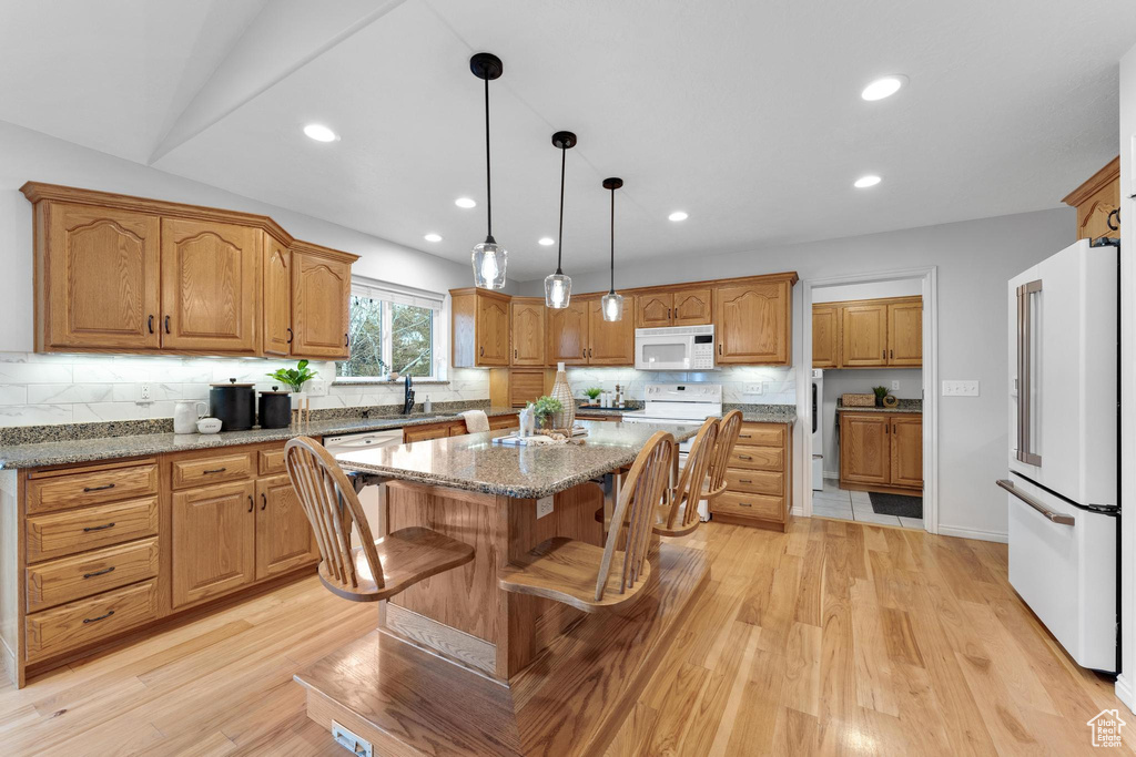 Kitchen with a center island, light stone countertops, light hardwood / wood-style floors, and white appliances