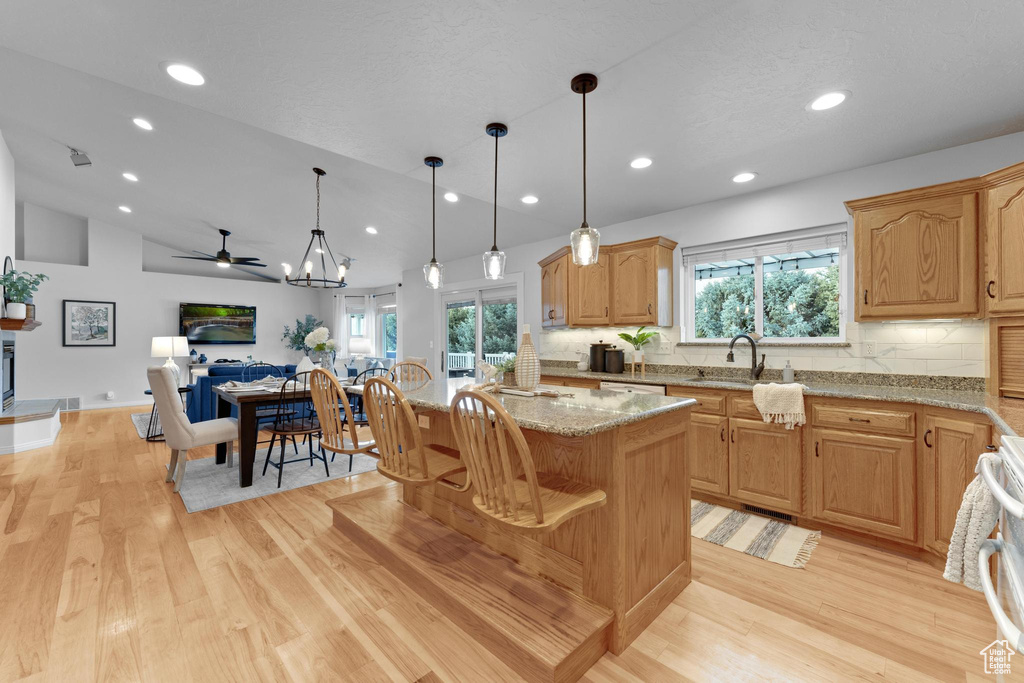 Kitchen featuring backsplash, ceiling fan with notable chandelier, light hardwood / wood-style flooring, and light stone counters