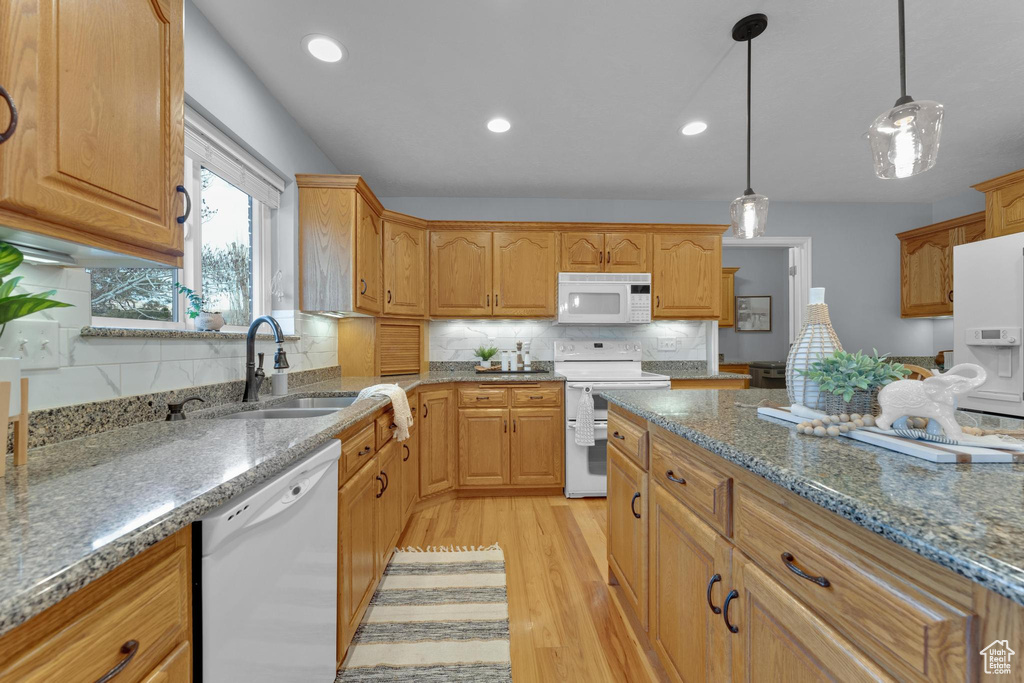 Kitchen with light hardwood / wood-style floors, decorative light fixtures, white appliances, backsplash, and sink