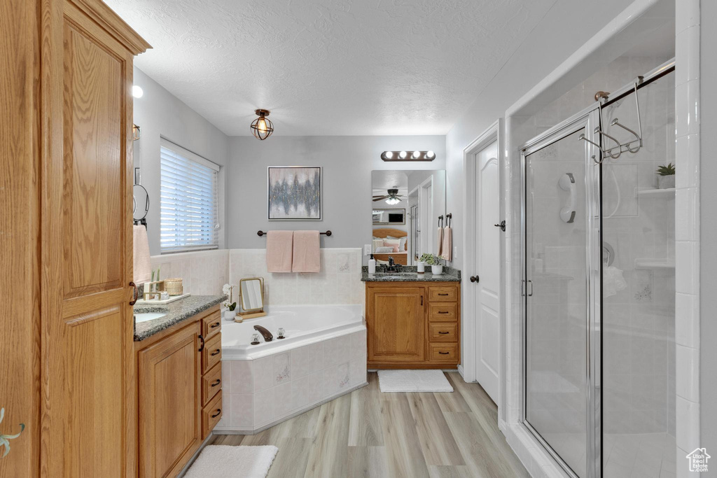 Bathroom with ceiling fan, wood-type flooring, a textured ceiling, separate shower and tub, and oversized vanity
