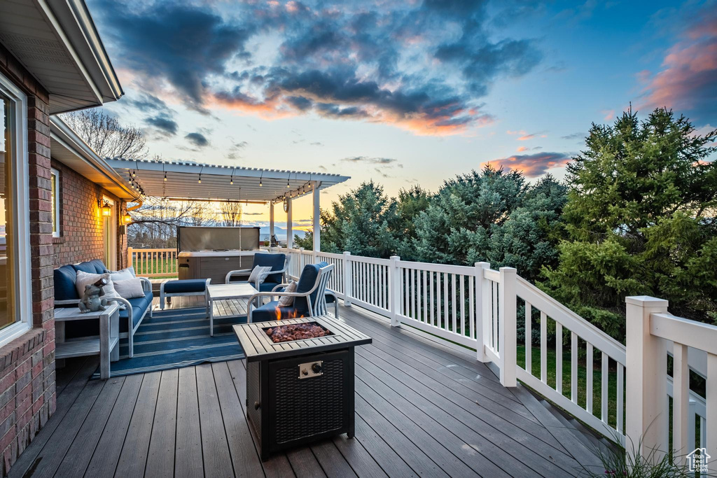 Deck at dusk featuring a pergola and an outdoor living space with a fire pit