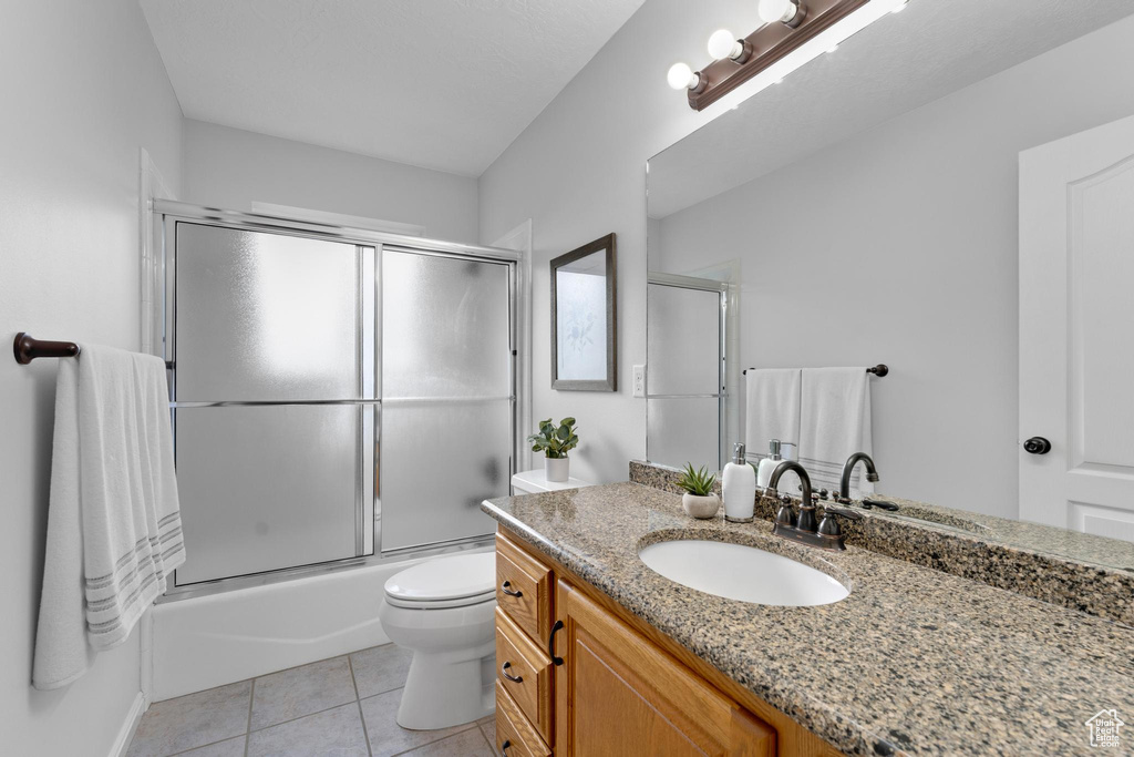 Full bathroom with toilet, combined bath / shower with glass door, tile floors, and vanity
