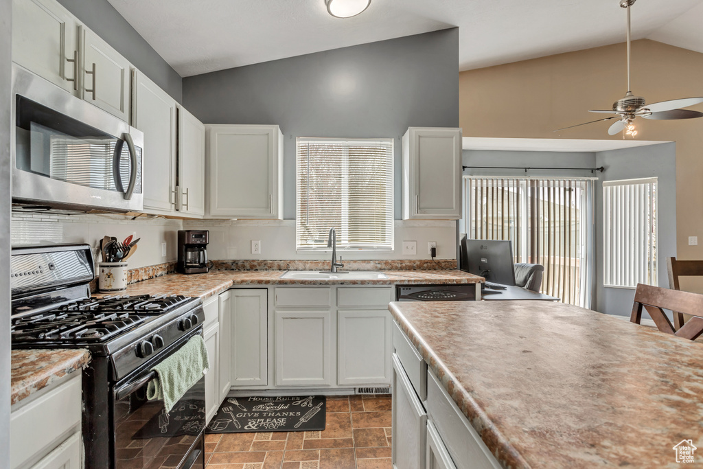 Kitchen with light tile flooring, ceiling fan, black gas range oven, white cabinets, and sink