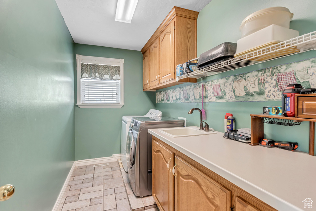 Laundry room with washer and clothes dryer, cabinets, sink, and light tile floors