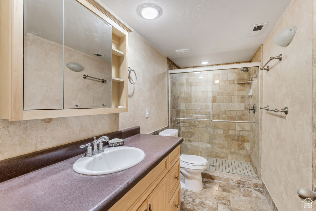 Bathroom featuring tile floors, toilet, large vanity, and walk in shower
