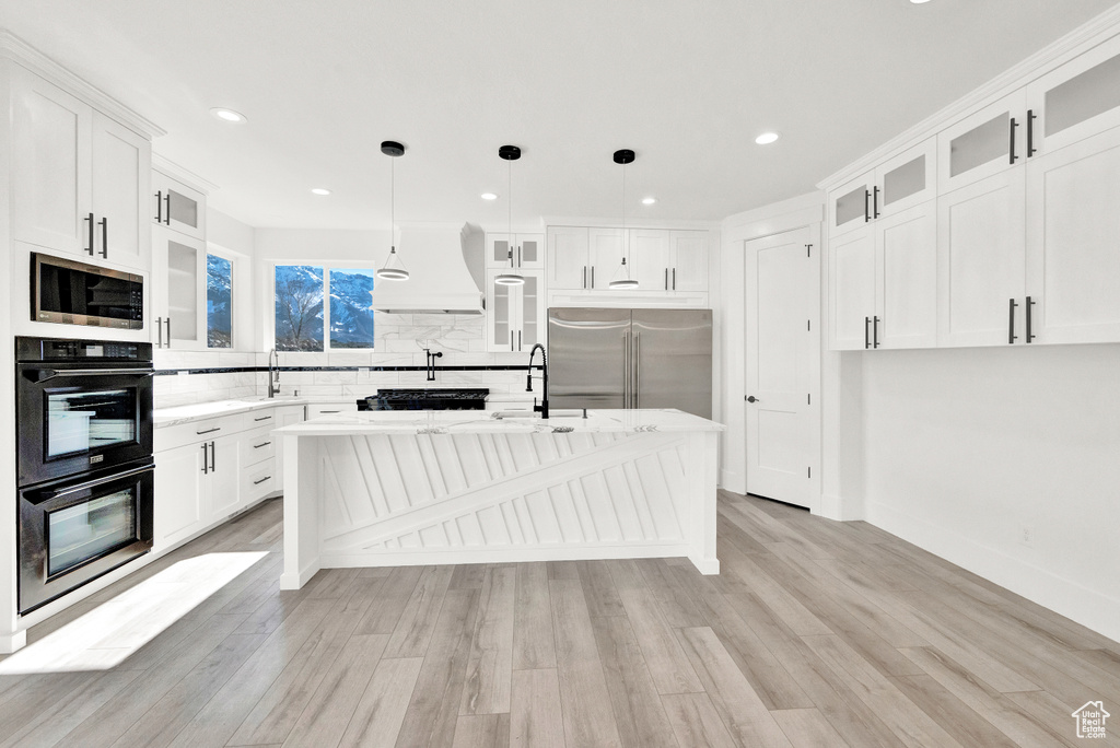 Kitchen with pendant lighting, built in appliances, light hardwood / wood-style floors, and white cabinets