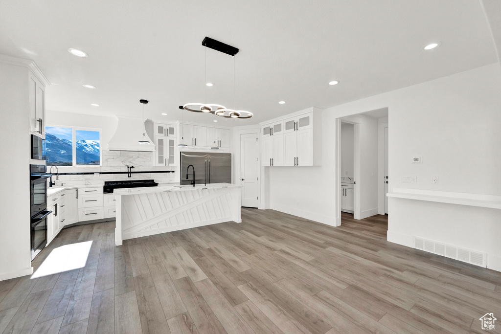 Kitchen featuring premium range hood, high quality fridge, white cabinets, hanging light fixtures, and a kitchen island with sink