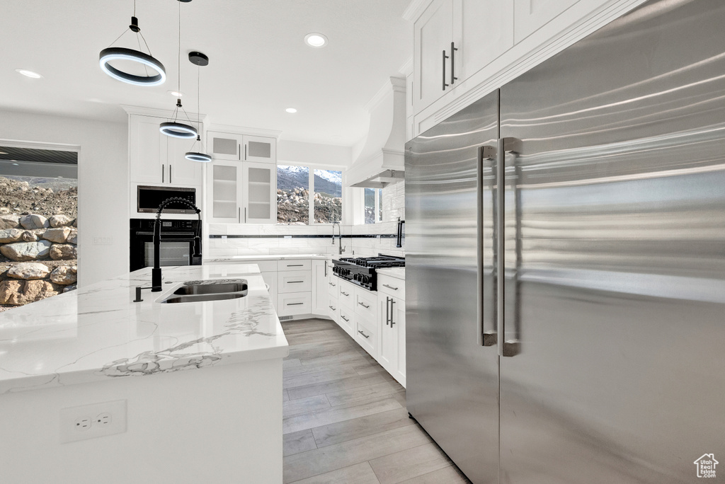 Kitchen featuring tasteful backsplash, white cabinets, appliances with stainless steel finishes, and premium range hood