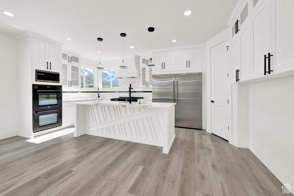 Kitchen featuring white cabinets, pendant lighting, built in appliances, and light hardwood / wood-style flooring