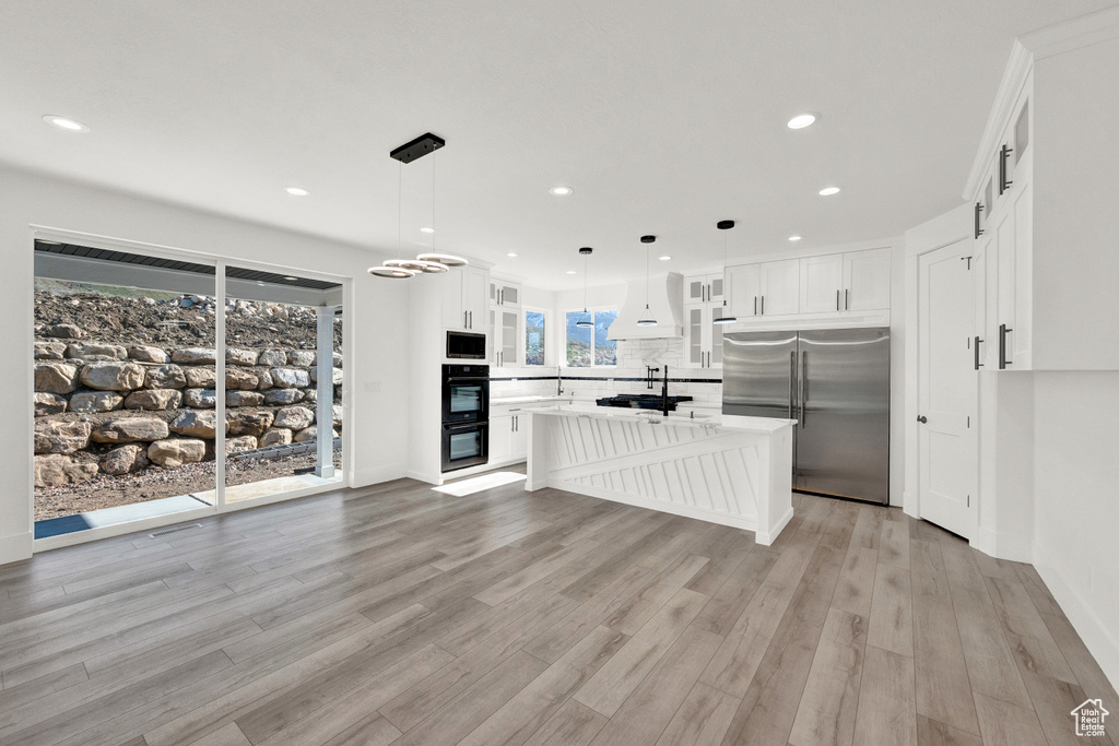 Kitchen with decorative light fixtures, backsplash, white cabinets, a center island, and built in appliances