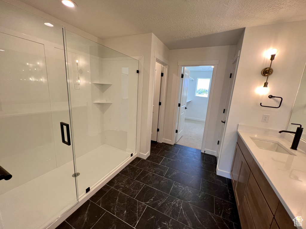 Bathroom featuring dual bowl vanity, tile flooring, a shower with shower door, and a textured ceiling