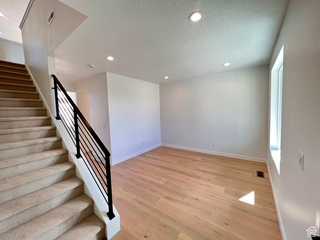 Stairs with light hardwood / wood-style flooring and a textured ceiling