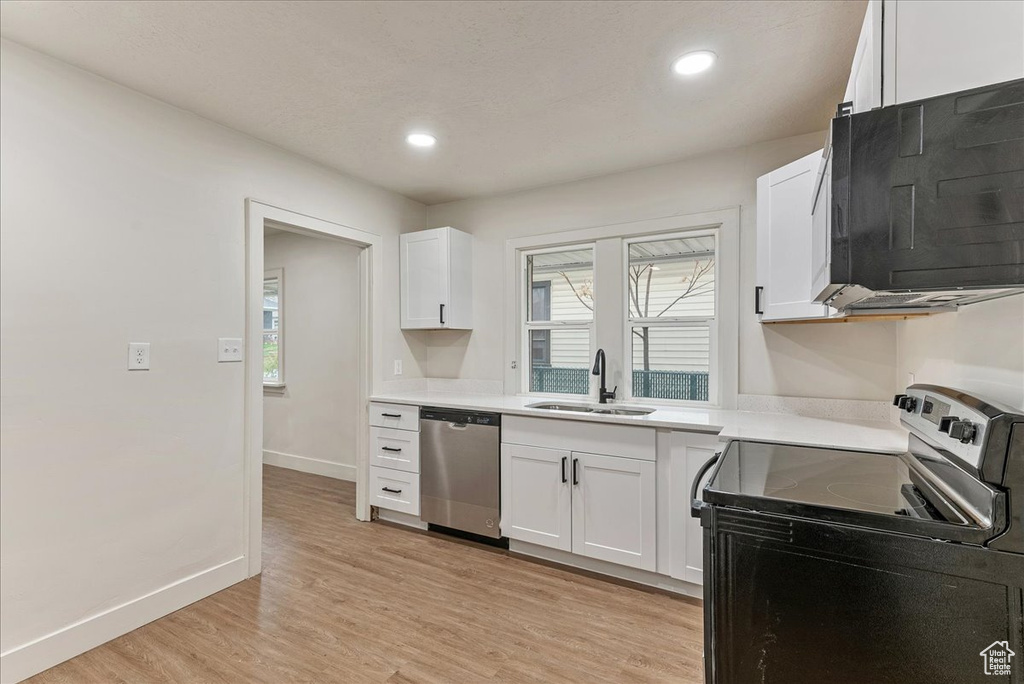 Kitchen with white cabinets, stainless steel appliances, light wood-type flooring, and sink