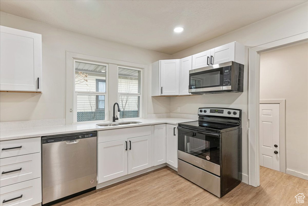 Kitchen with light hardwood / wood-style flooring, white cabinetry, appliances with stainless steel finishes, and sink