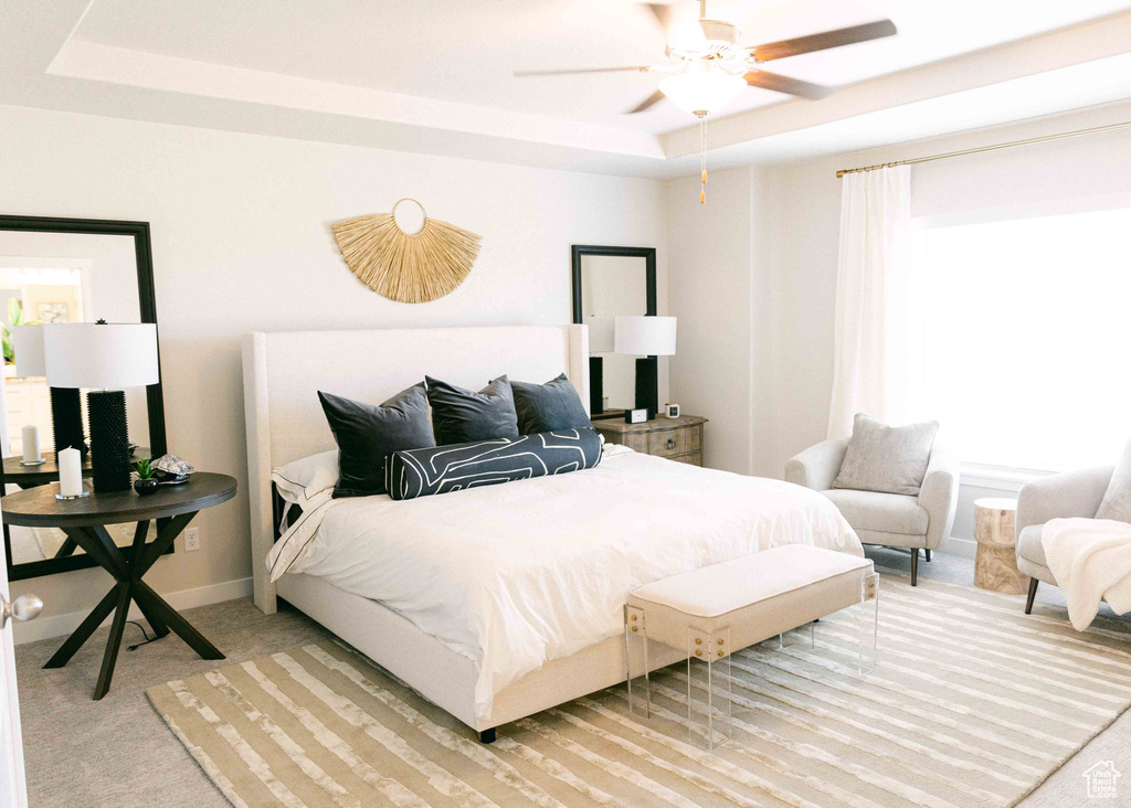 Bedroom with light colored carpet, a raised ceiling, and ceiling fan