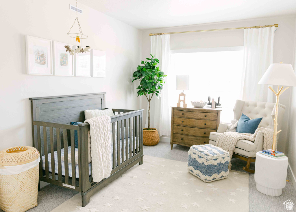 Carpeted bedroom featuring a chandelier and a nursery area