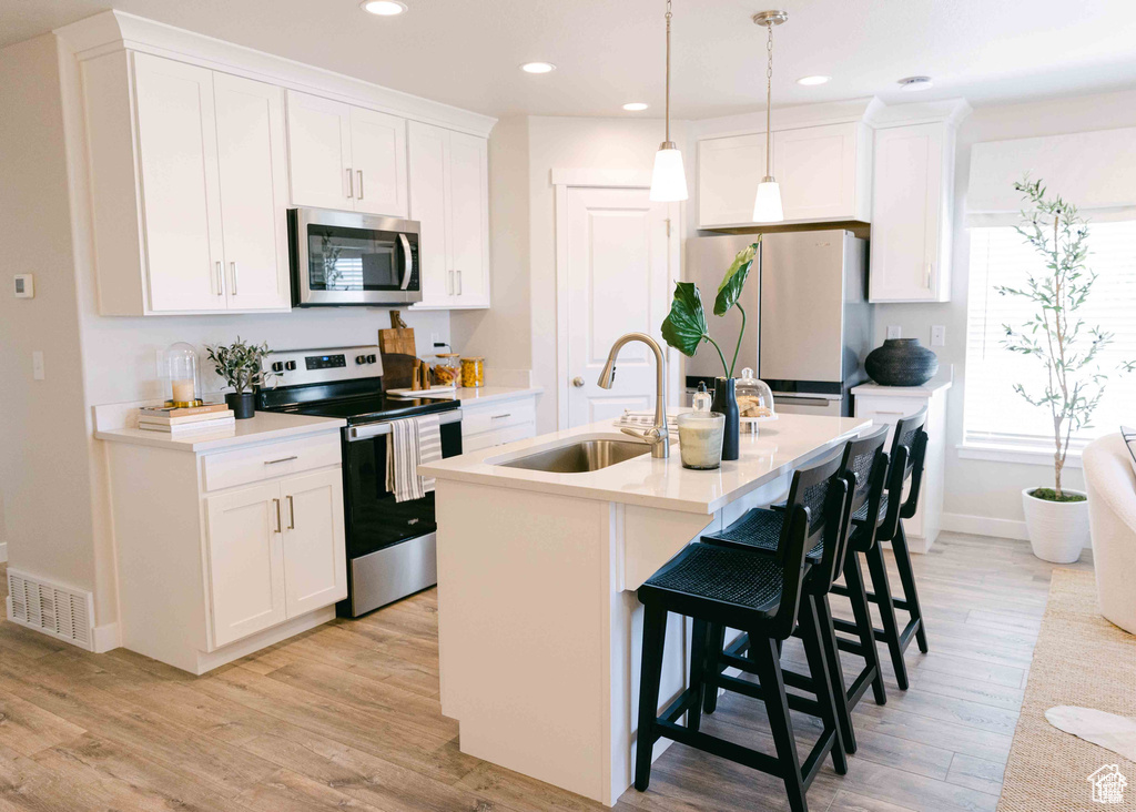 Kitchen featuring light hardwood / wood-style floors, stainless steel appliances, a breakfast bar area, a kitchen island with sink, and sink