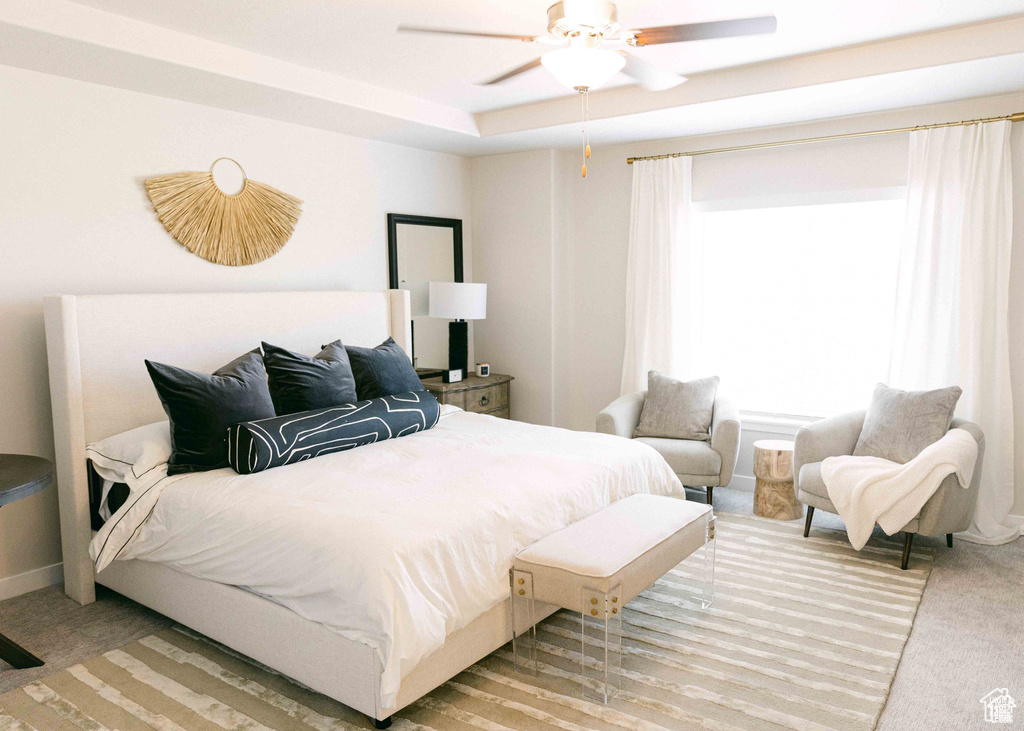 Bedroom featuring light carpet, ceiling fan, and a tray ceiling