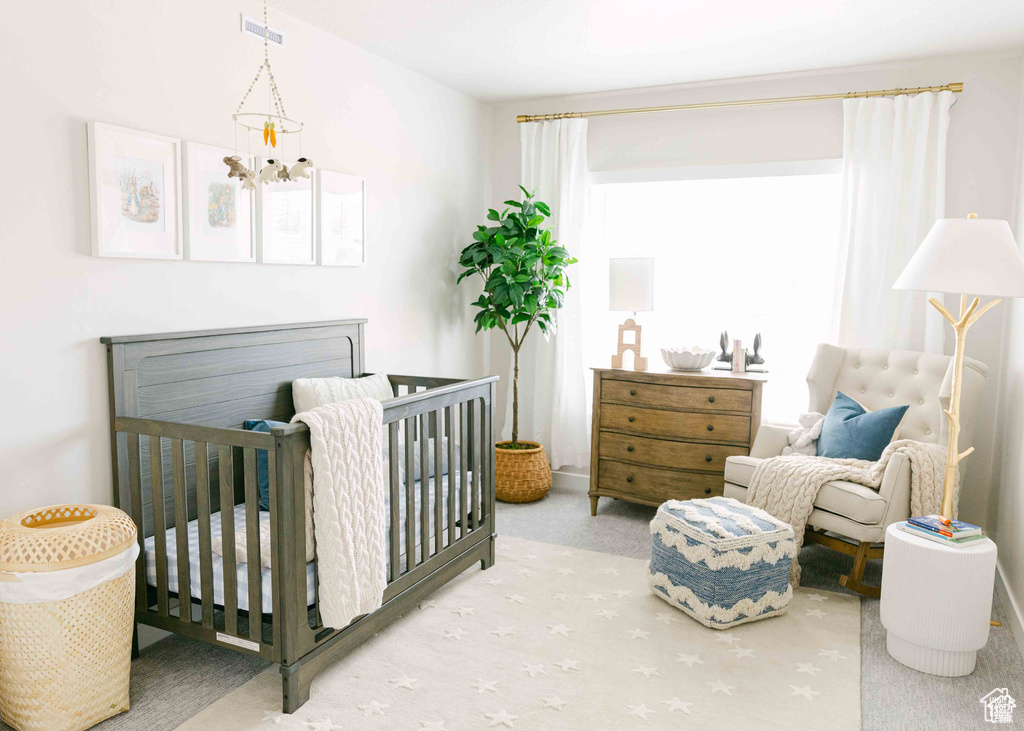 Carpeted bedroom featuring a nursery area and an inviting chandelier