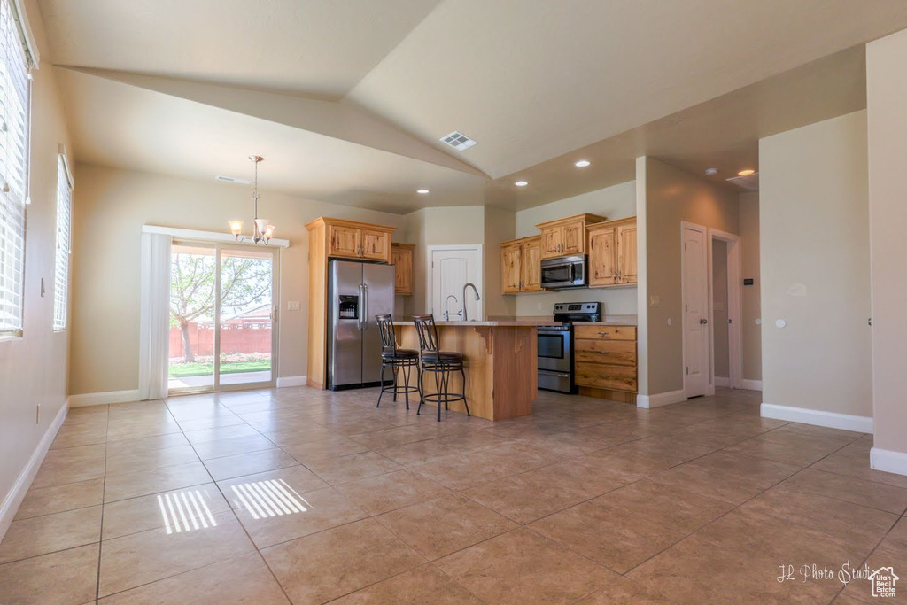 Kitchen with an island with sink, light tile floors, a kitchen breakfast bar, appliances with stainless steel finishes, and a notable chandelier