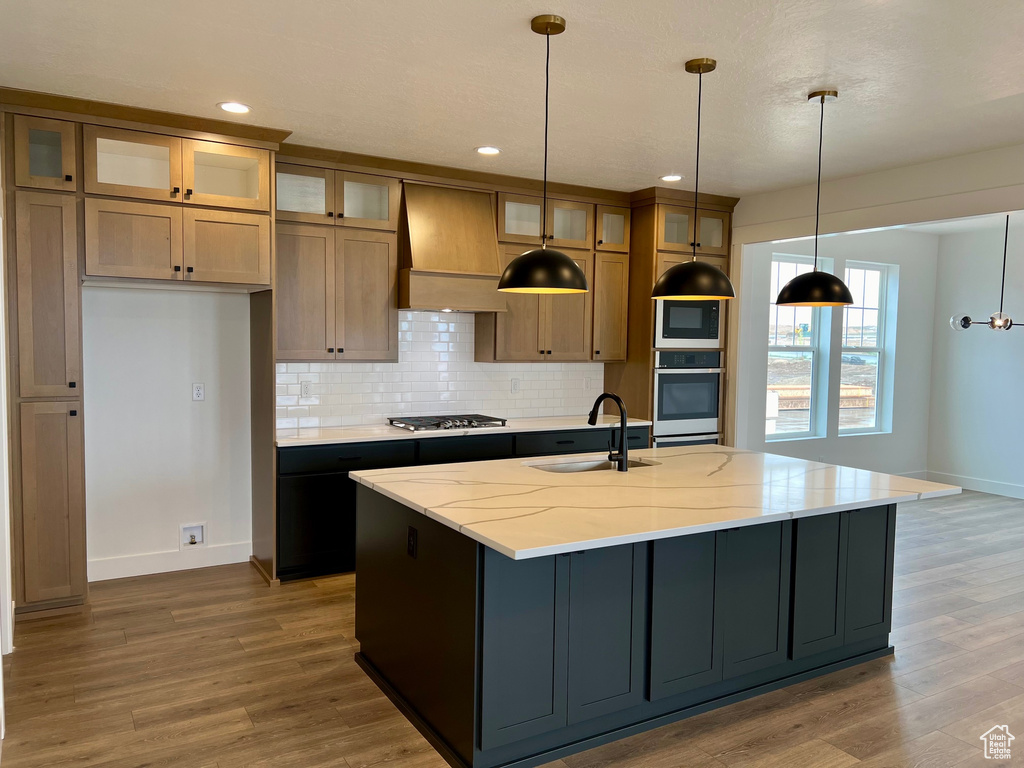 Kitchen with hardwood / wood-style flooring, appliances with stainless steel finishes, custom range hood, and an island with sink