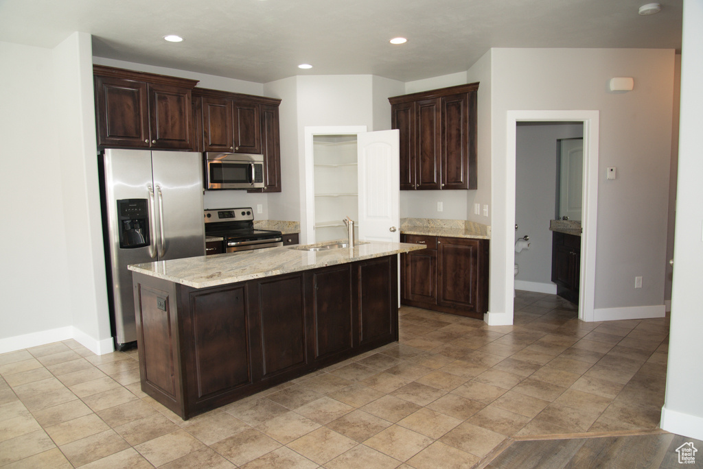 Kitchen with an island with sink, light stone countertops, stainless steel appliances, and light tile floors