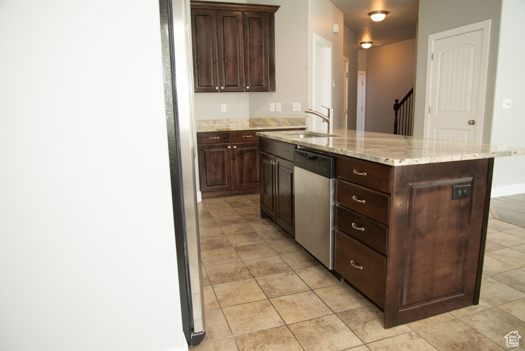Kitchen featuring sink, light tile floors, light stone counters, dishwasher, and dark brown cabinets