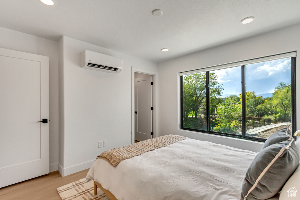 Bedroom with a wall mounted air conditioner and light hardwood / wood-style floors