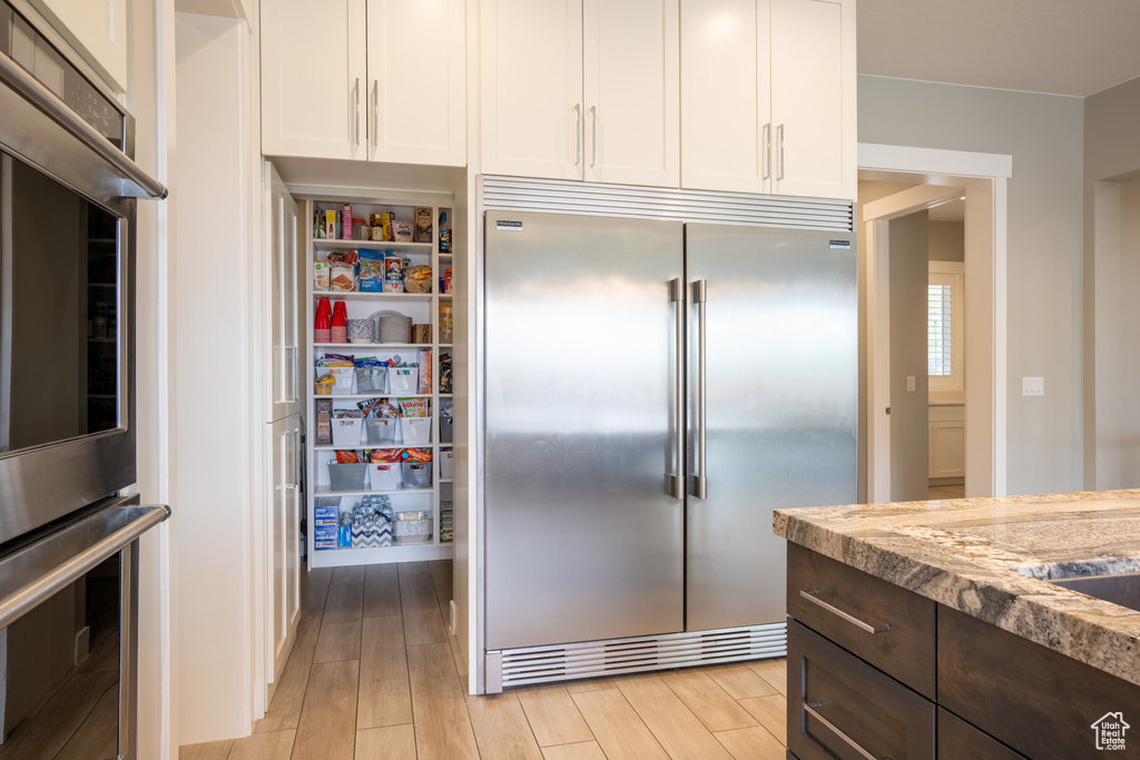 Interior space featuring light hardwood / wood-style floors, white cabinets, appliances with stainless steel finishes, and dark brown cabinetry