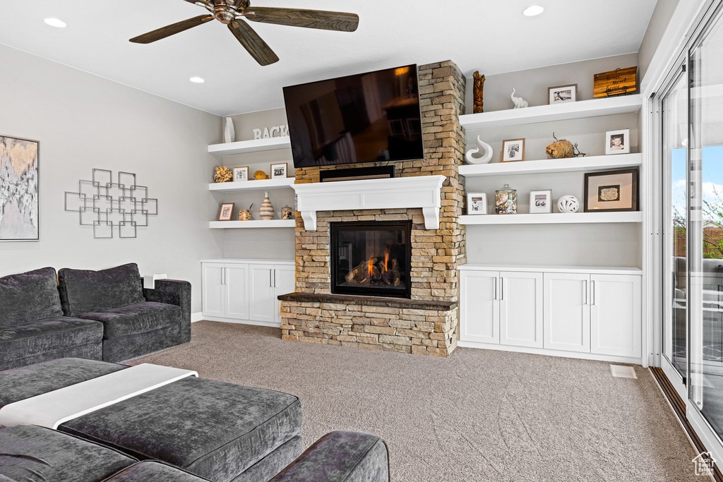 Carpeted living room featuring a stone fireplace and ceiling fan