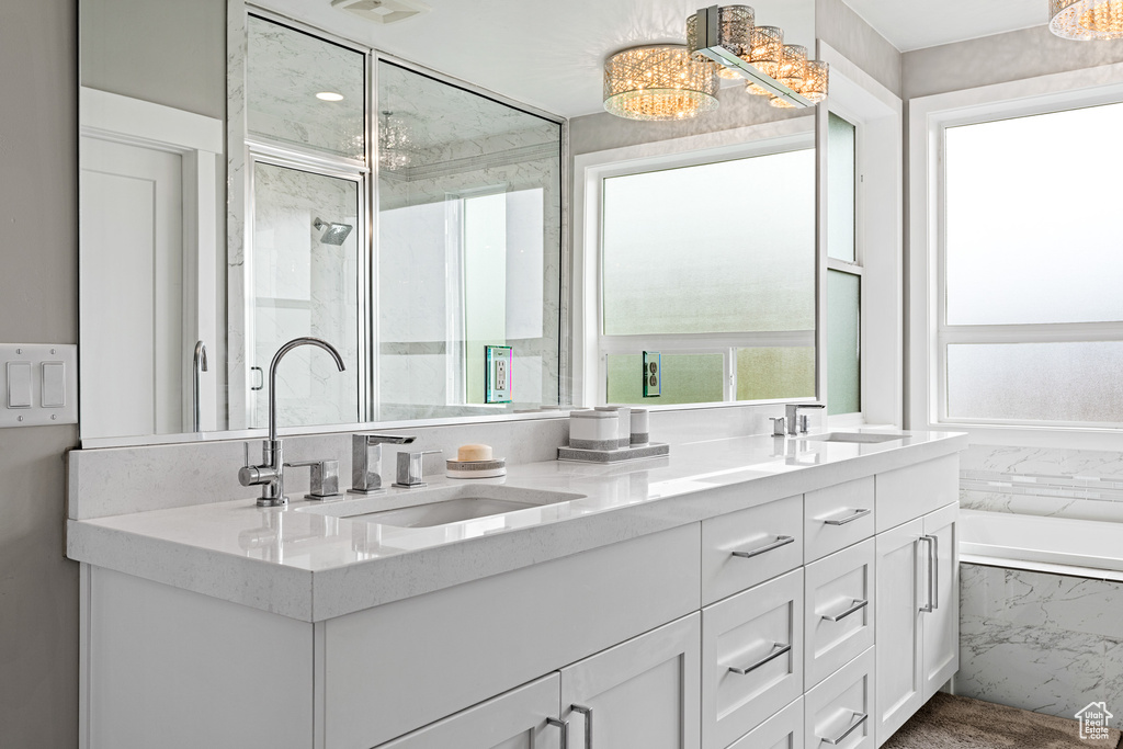 Bathroom featuring an inviting chandelier, double sink, vanity with extensive cabinet space, and tiled bath