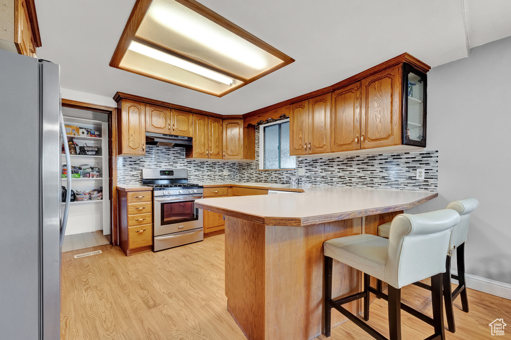 Kitchen with a kitchen breakfast bar, appliances with stainless steel finishes, backsplash, and light wood-type flooring
