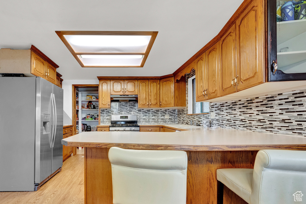 Kitchen featuring kitchen peninsula, backsplash, a breakfast bar, light hardwood / wood-style floors, and stainless steel appliances