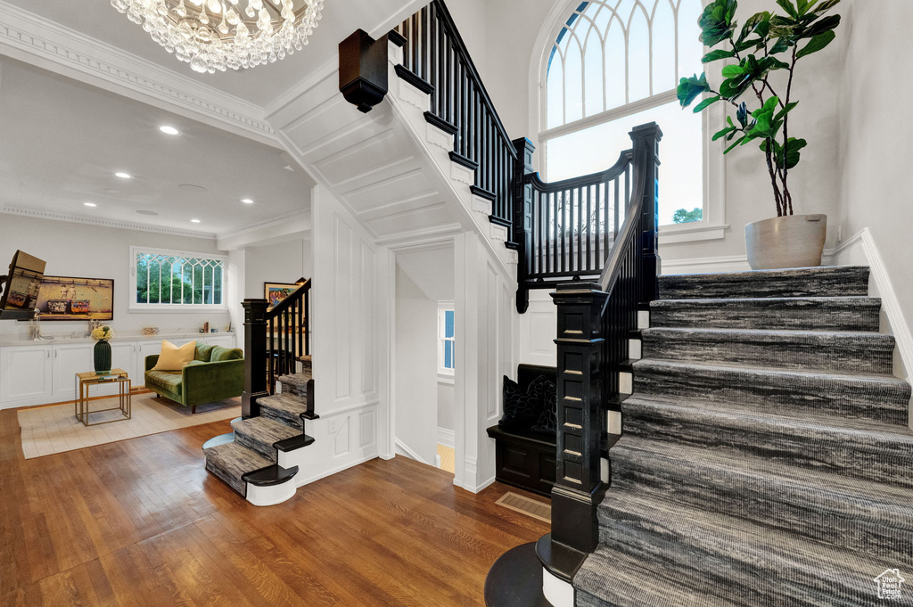 Staircase featuring a high ceiling, a notable chandelier, crown molding, and hardwood / wood-style flooring