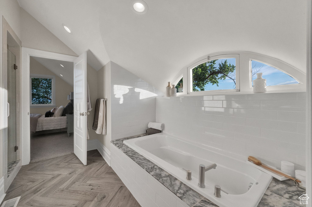 Bathroom featuring lofted ceiling, independent shower and bath, parquet floors, and tile walls