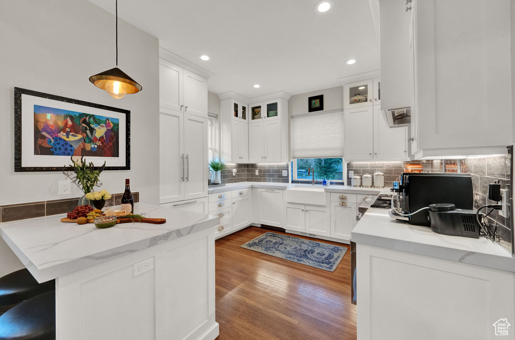 Kitchen with light hardwood / wood-style floors, decorative light fixtures, white cabinets, and tasteful backsplash