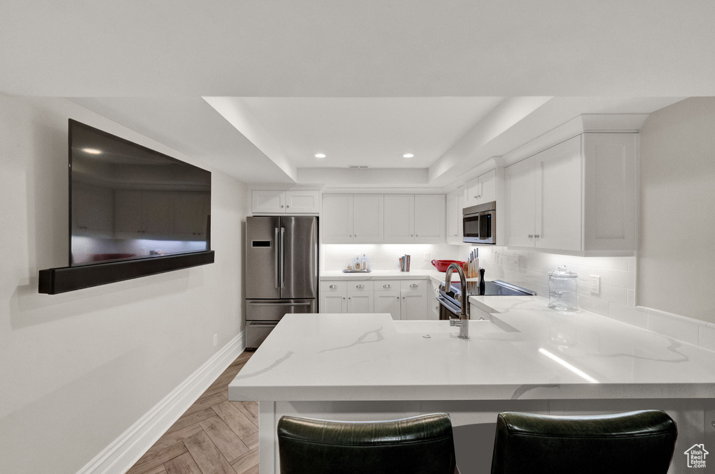 Kitchen with light parquet floors, stainless steel appliances, white cabinets, and a breakfast bar