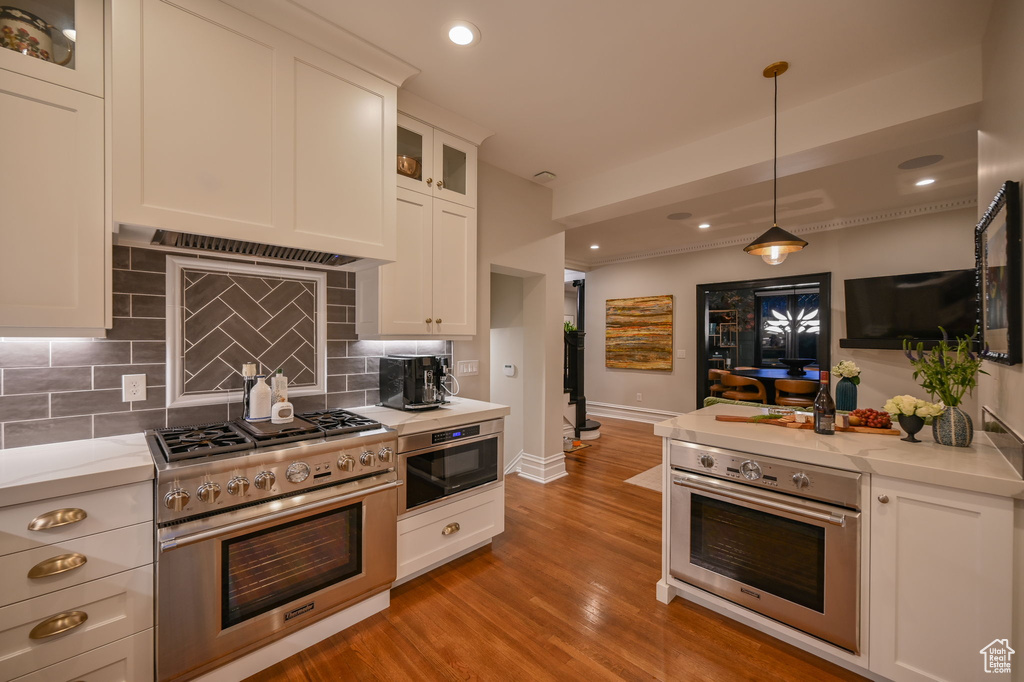 Kitchen with white cabinetry, appliances with stainless steel finishes, light hardwood / wood-style flooring, tasteful backsplash, and pendant lighting
