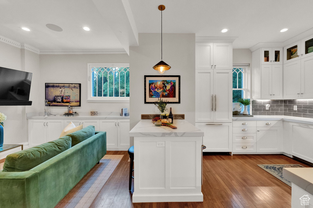 Kitchen with pendant lighting, light stone counters, light hardwood / wood-style flooring, tasteful backsplash, and white cabinetry