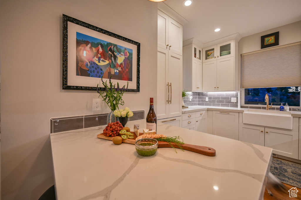 Kitchen with kitchen peninsula, sink, light stone counters, white cabinets, and backsplash