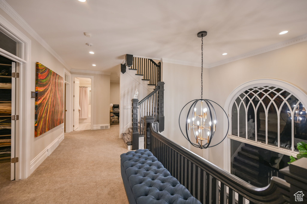 Hall with an inviting chandelier, ornamental molding, and light colored carpet