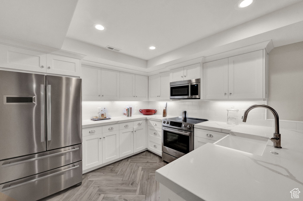 Kitchen with backsplash, sink, stainless steel appliances, white cabinets, and light parquet flooring