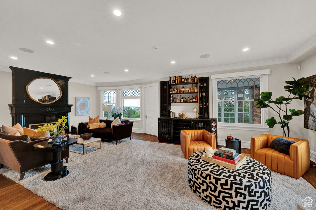 Living room with indoor bar, hardwood / wood-style floors, a large fireplace, and crown molding