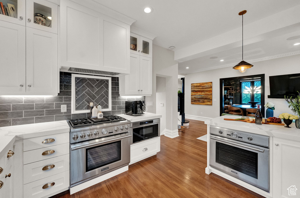 Kitchen with light stone counters, appliances with stainless steel finishes, tasteful backsplash, white cabinetry, and light wood-type flooring