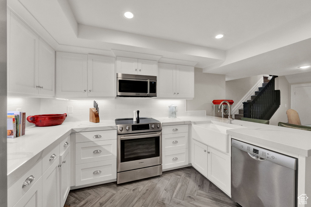 Kitchen with light parquet flooring, white cabinets, stainless steel appliances, and sink