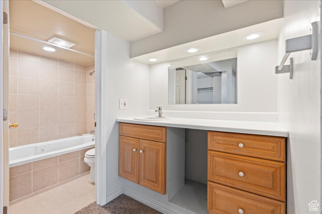 Full bathroom with tiled shower / bath, toilet, vanity with extensive cabinet space, and tile flooring