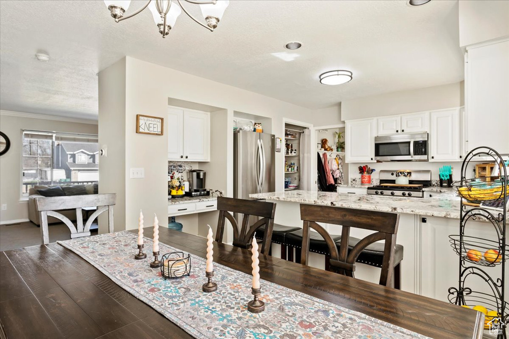 Kitchen featuring white cabinets, appliances with stainless steel finishes, a chandelier, and light stone counters